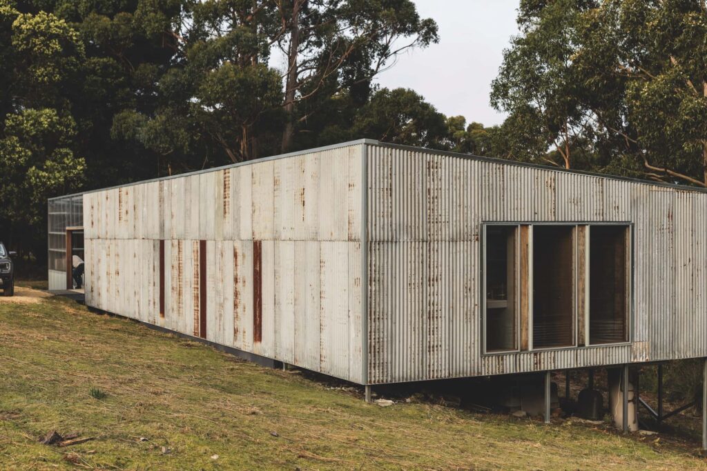 Exterior view showing the weathered corrugated iron form nestled between eucalypts, photographed for issue 107: Assemblage by Adam Gibson.