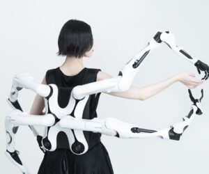 Person wearing a white multi-jointed robotic exoskeleton with articulated arms extending outward.