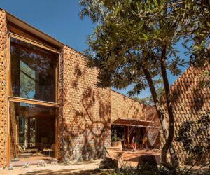 House clad in handcrafted terracotta tiles with deep window openings set within a coastal landscape.