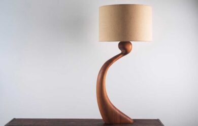 Curved timber table lamp by Margot Feast with a fabric lampshade on a dark wooden table.