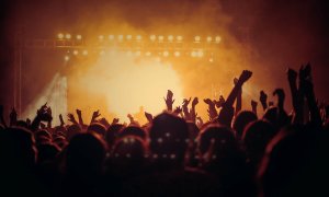 A backlit shot of a crowd with their hands raised facing a concert stage.