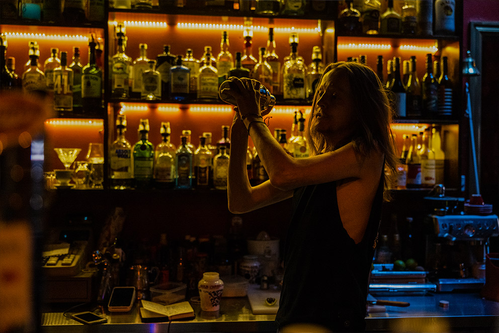 Night time shot of a barman mixing a cocktail, backlit with bottles of alcohol