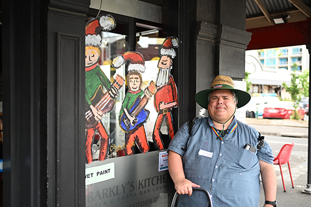 Artist painting on a shopfront window for the festive season 2024, as a part of the Festive Art on Windows program, in the Sydney Road Brunswick precinct.