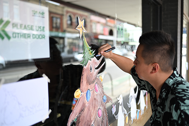 Artist painting on a shopfront window for the festive season 2024, as a part of the Festive Art on Windows program, in the Sydney Road Brunswick precinct.