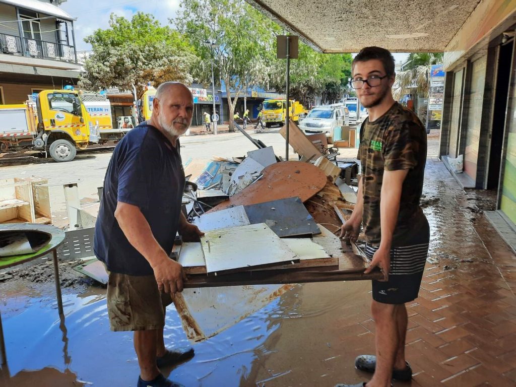 Two male ADRA volunteers, one older and one younger, cleaning up flood debris