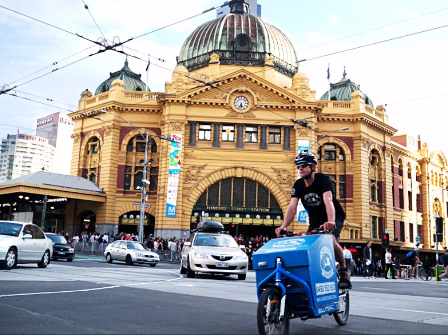 Photo of Flinders Street Station and a man on a bike with a delivery box at the front.