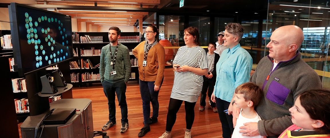 Four adults standing in a line looking at a tv screen that has dots on it.