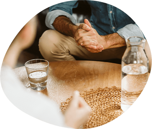 A clinical psychologist and client sit opposite one another across a table, in therapy