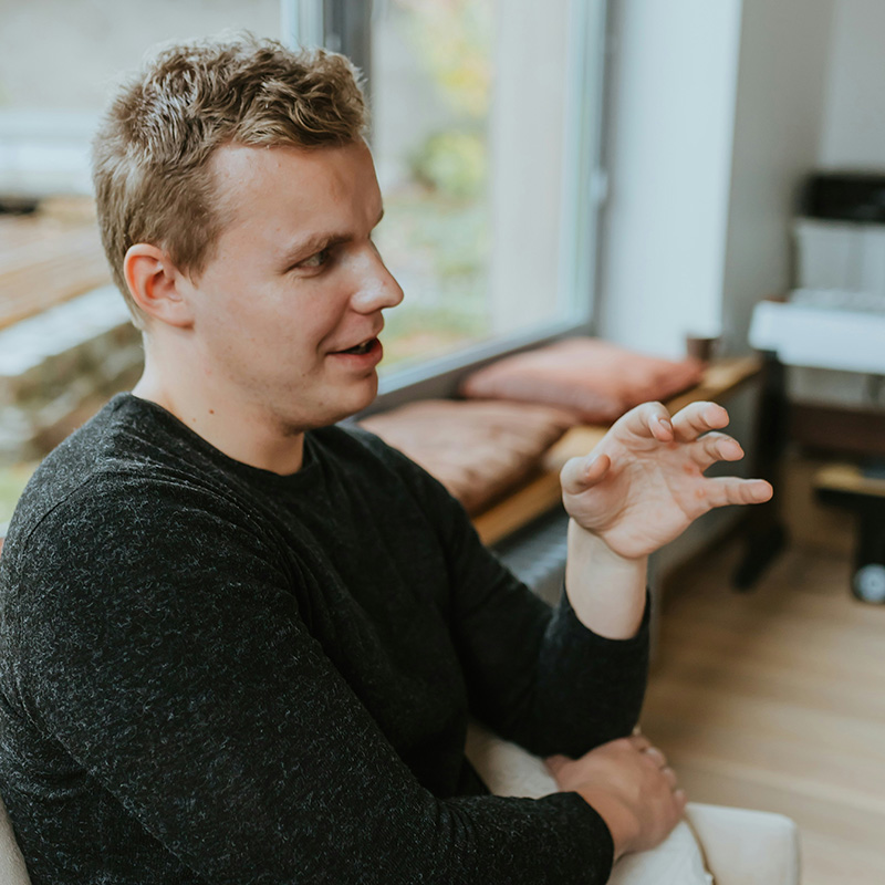A man sits on a sofa in therapy, gesturing with hsi hand as he speaks