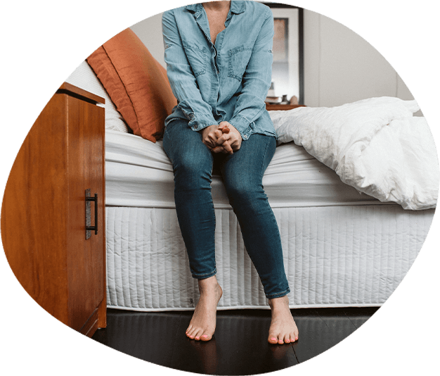 A woman sits on the edge of a bed with bare feet on the ground
