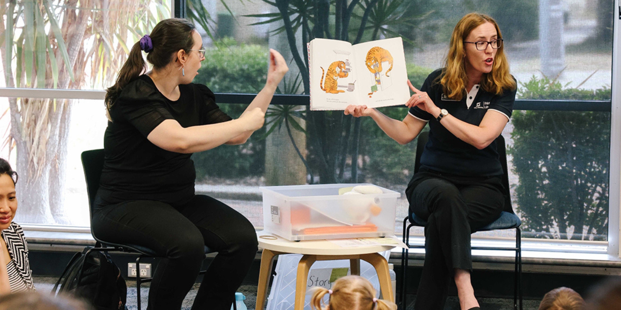 Auslan Story Time in Osborne Park with the City of Stirling and Deaf Connect banner. The banner consists of an image of two women sitting on chairs in front of a group of children. One is holding a book up and the other is communicating through Auslan