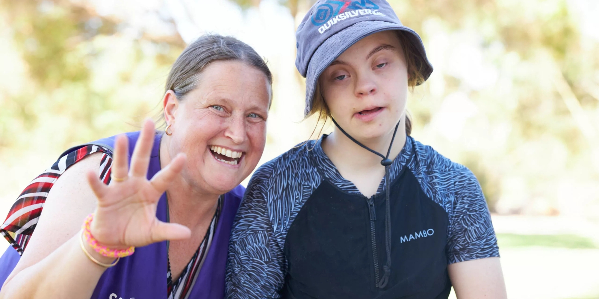 Cahoots Winter School Holiday Camps banner. The banner consists of an image of a cahoots staff members waving at the camera and smiling, standing next to a participant who is wearing a hat and black swiming top