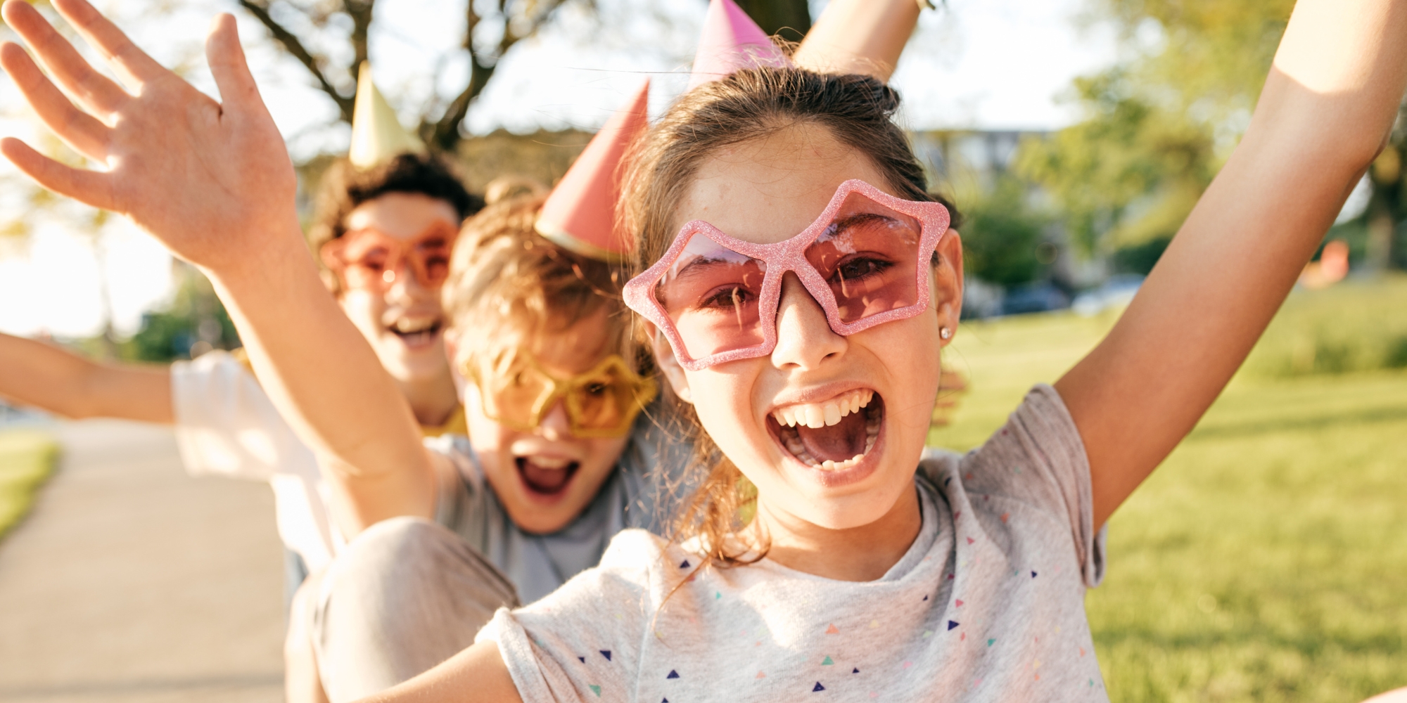 July Telethon Holiday Makers Program with Spectrum Space banner. The banner consists of an image of a groups of children with their arms up, cheering and smiling at the camera. The girl in the front is wearing a grey shirt with star staped sunglasses. They are outside with grass in the background