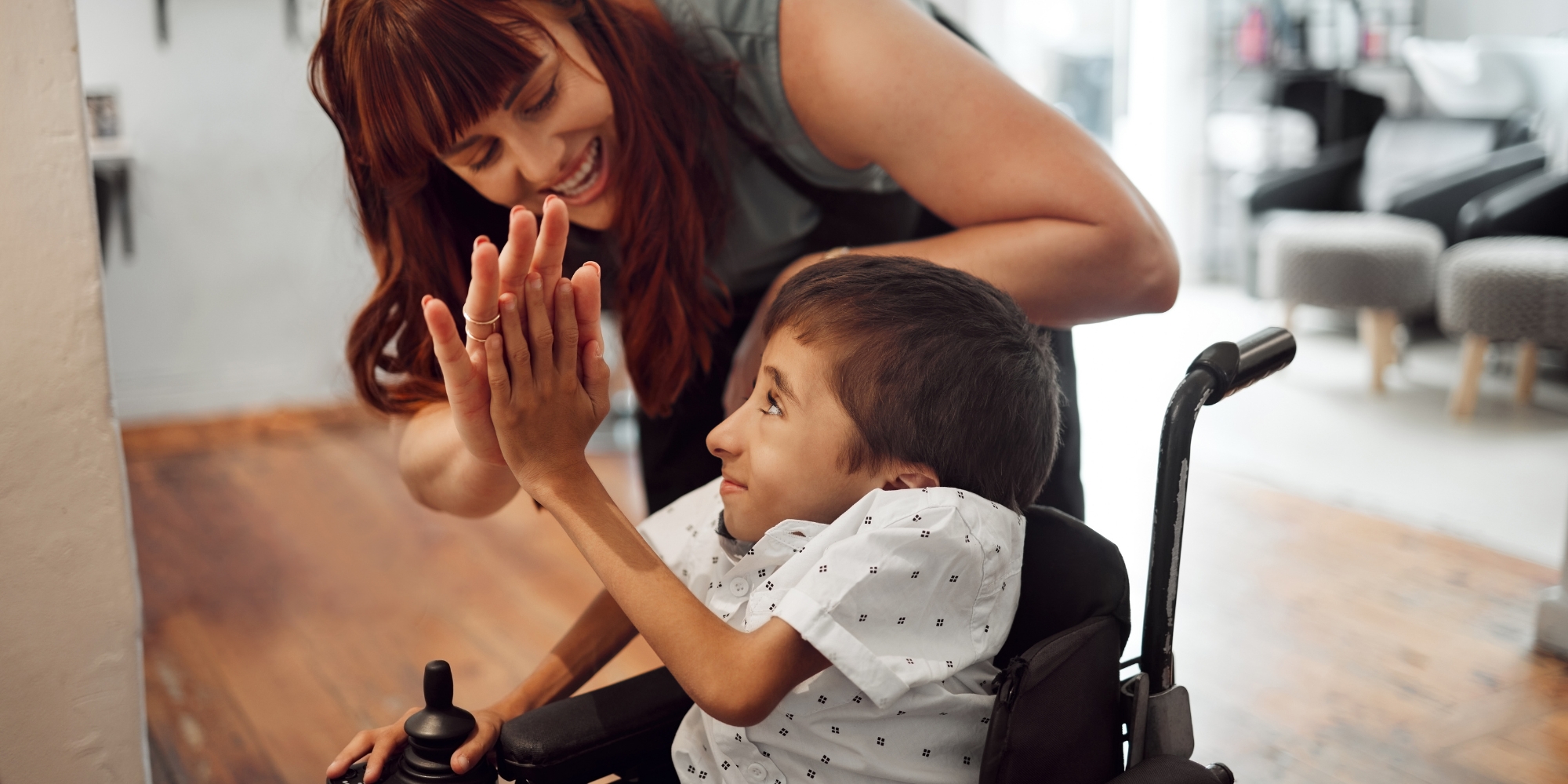 WA Carers Strategy 2025 with the State Government banner. The banner consists of an image of a woman leaning over and high five-ing a boy who is sitting in a wheelchair. They are both smiling at each other and are in a home.