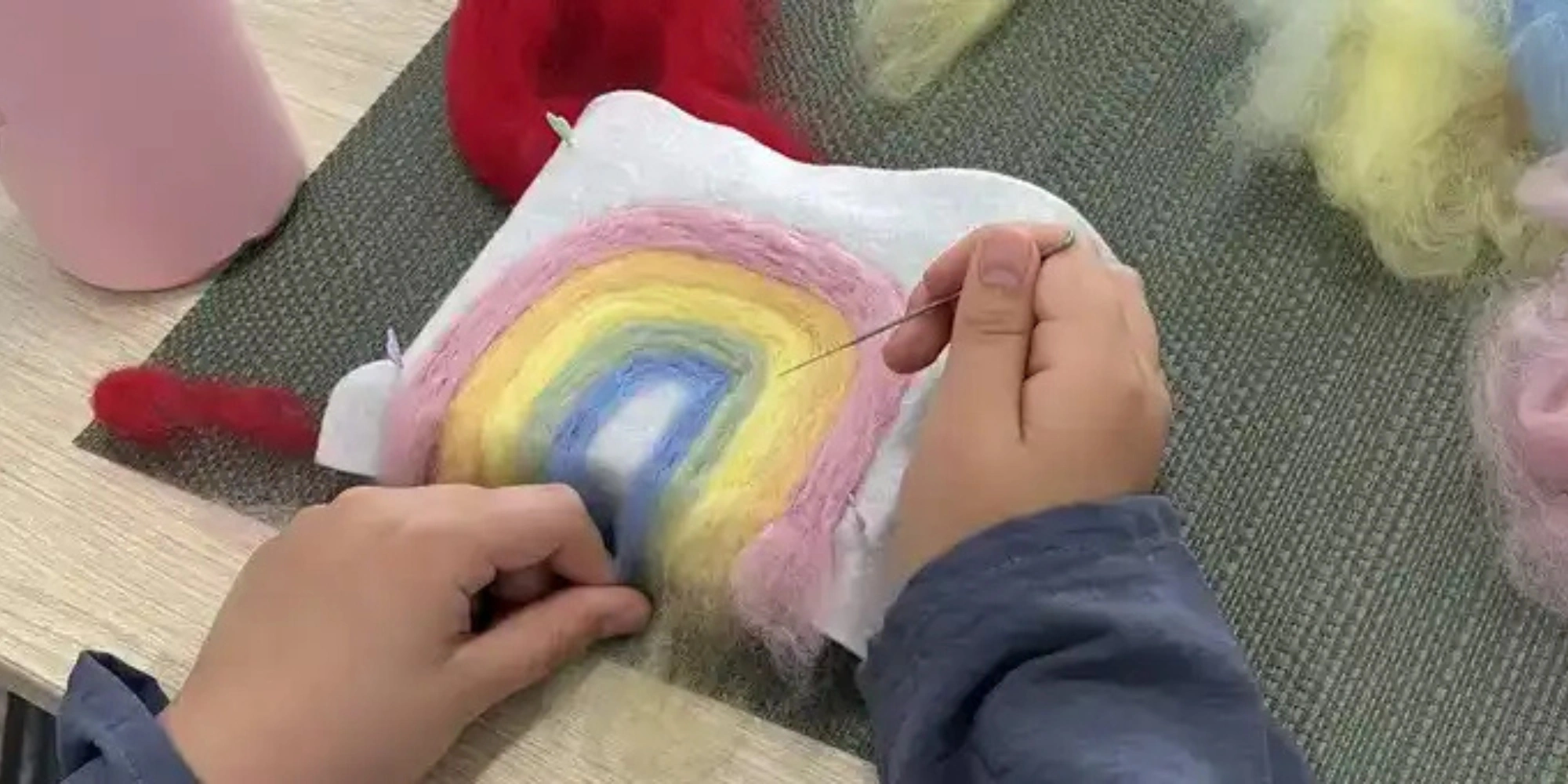 Home School Needle Felting Family Class with The Victoria Park Community Centre and Solstice Fibre banner. The banner consists of an image of a child holding a needle and working on a felt rainbow.