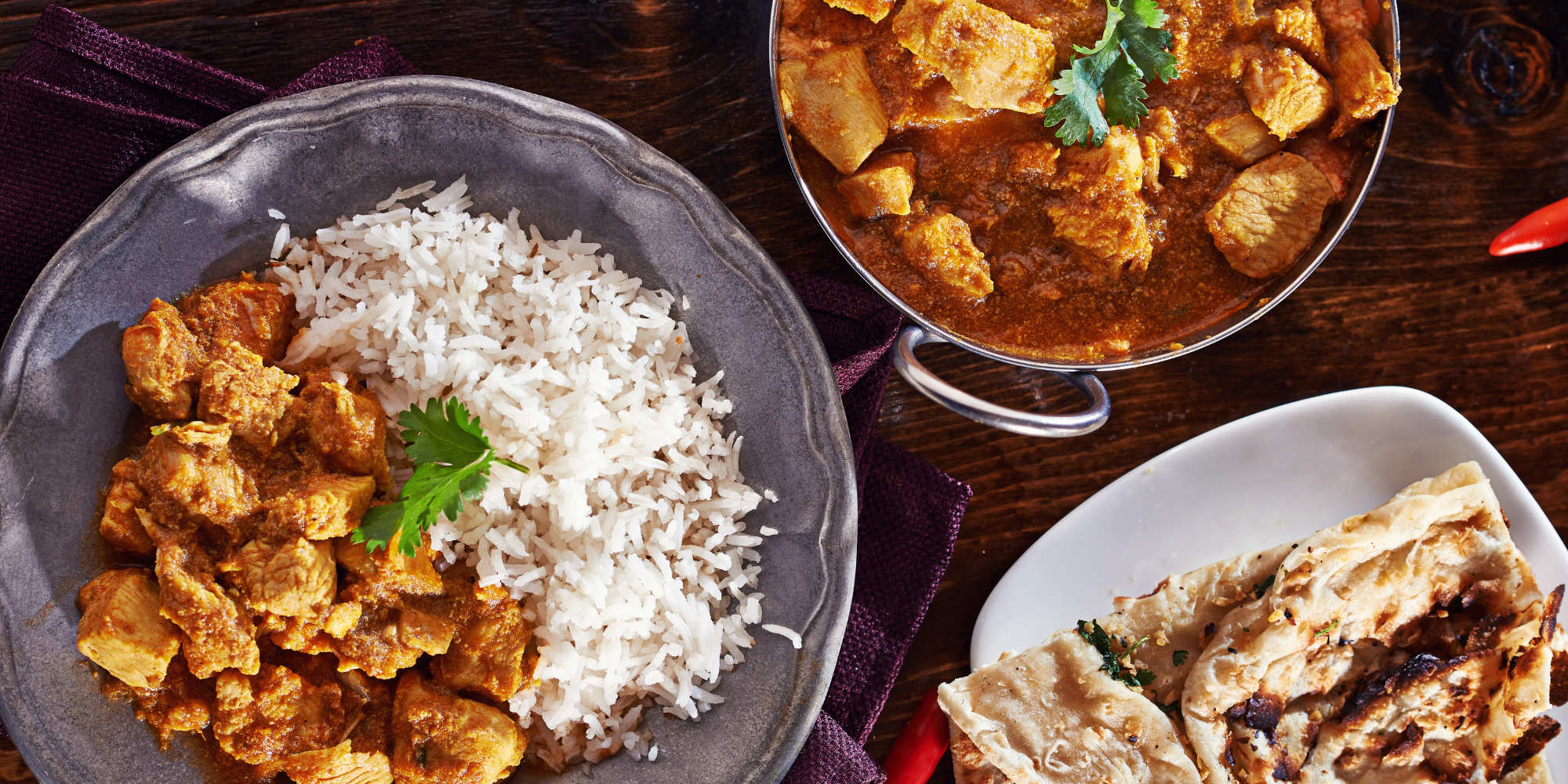 An image of three dishes with chicken curry, rice and naan bread