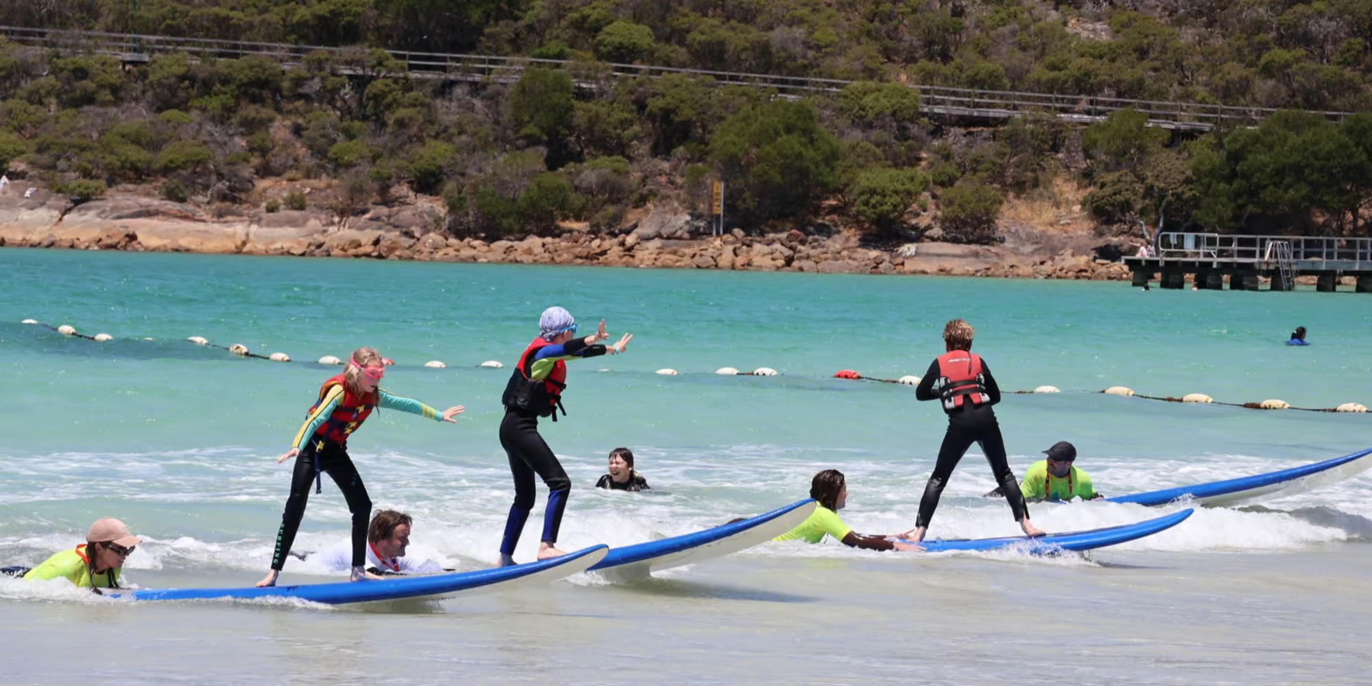 Three children on surfboards on the beach with instructors holding on to the tail of the surfboard