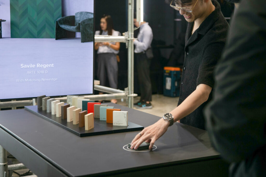 A Journey of Inspiration
The highlight of the evening was the premiere of Lamitak’s Thematic Video, followed by a presentation from Mr. Jansen Tan, Director of Product & Brand, who shared insights into the inspiration and design journey. “Great design begins with a good product. This collection merges modern urban spirit with the beauty of nature, inspired by road trips and explorations across the world. It is a journey of discovery that transforms into surfaces that feel both familiar and refreshingly new,” he explained.
Interactive Displays and Fun Activities
In Bangkok, the diversity of the collection came alive through an immersive exhibition. Massive hanging panels showcased the new laminates alongside photographs of their inspirations from around the world, giving context to each design story. The exhibition also underscored Lamitak’s respect for nature, simplicity and sustainability, with materials designed to be recyclable. Beyond the displays, interactivity took centre stage: at the Lamitak Scanner, we placed samples on a marked spot and watched product details flash up on screen — a simple yet surprisingly addictive way to engage with the collection. Nearby, guests tried their luck at the Good Gift vending machine, while artists at the Good Sketch corner illustrated portraits directly onto laminate panels. It was refreshing to see a brand embrace playful, interactive formats that turned product exploration into part of the party.