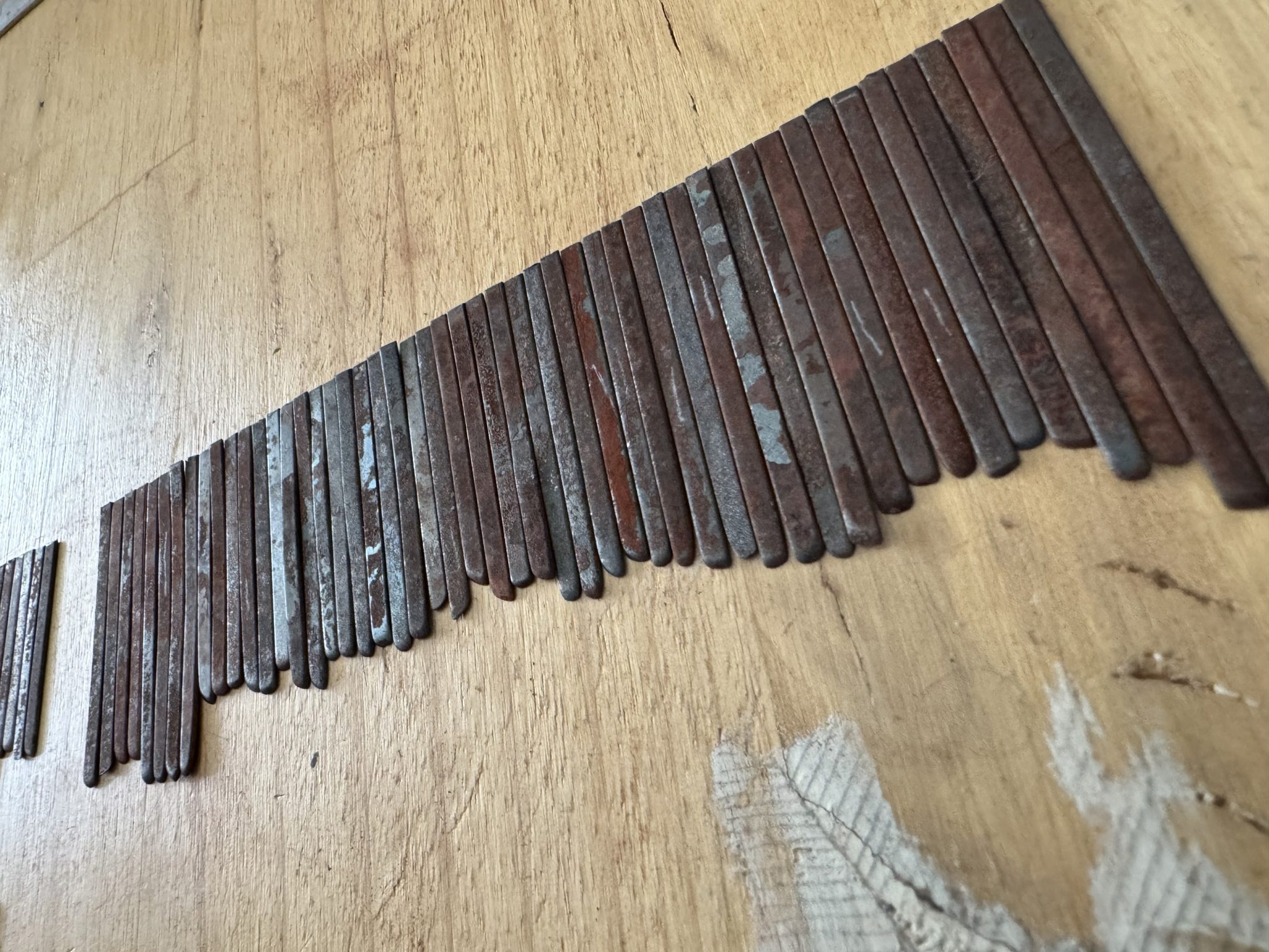 rusted steel street sweeper blade offcuts lined up in rough height order on a wood surface