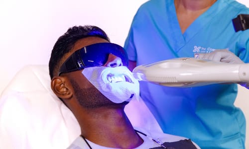 Male client receiving professional teeth whitening treatment with light focused on his teeth.