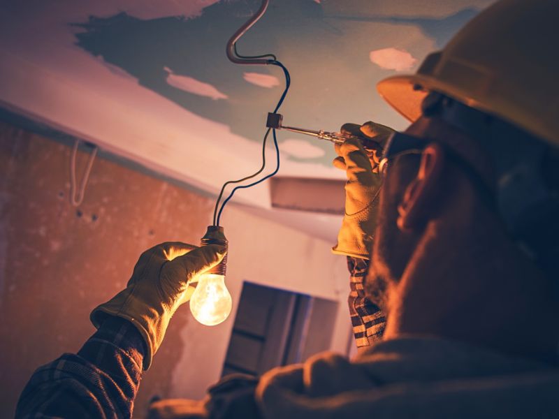 Electricians holding bulb and inspecting wire