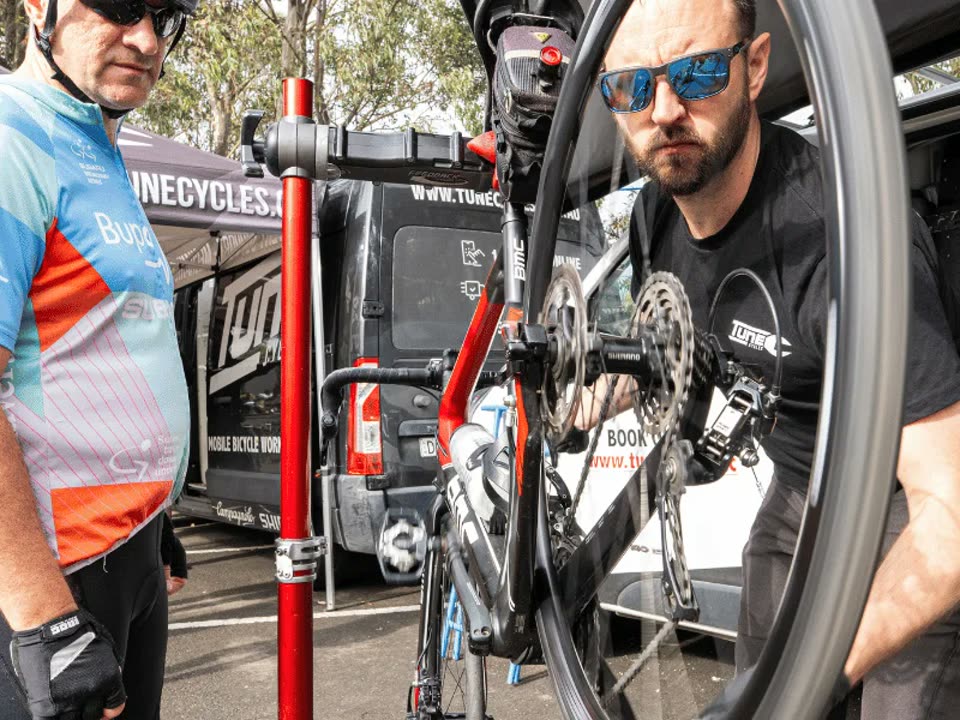 Tune Cycles mechanic servicing a road bike in a repair stand beside the mobile workshop van