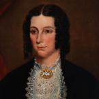 Oil painting of a woman wearing a lace collar, elaborate gold brooch with curls arrange on either side of her face.