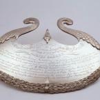 An ornate shiny silver crest with extensive text engraving