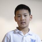 A young boy wearing a white polo shirt with a blue school logo.