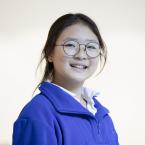 A young girl with round glasses, wearing a blue jacket.