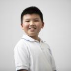 A boy smiling at the camera, wearing a white polo shirt.