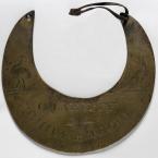 A crescent shaped piece of dull brass with words and images carved into it
