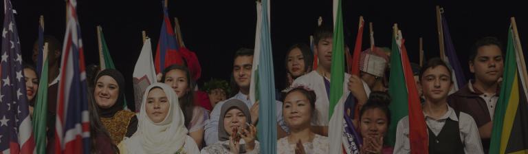 A group of students wearing national costumes and waving national flags.